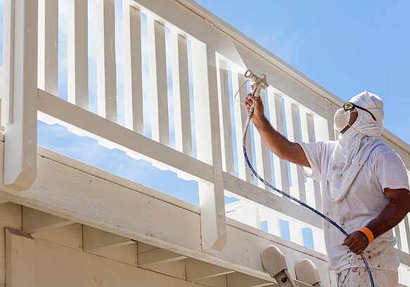 House Painter Wearing Facial Protection Spray Painting A Deck of A Home.