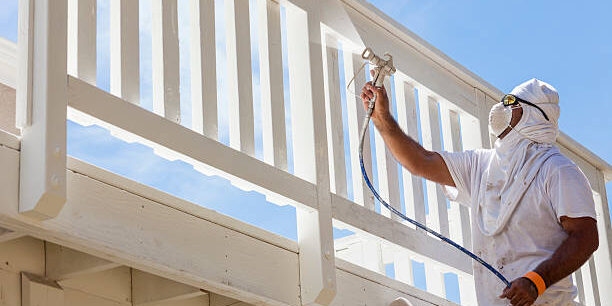 House Painter Wearing Facial Protection Spray Painting A Deck of A Home.