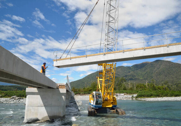 Builders construct a concrete bridge over a small river in Westland, New Zealand