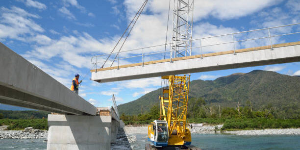 Builders construct a concrete bridge over a small river in Westland, New Zealand