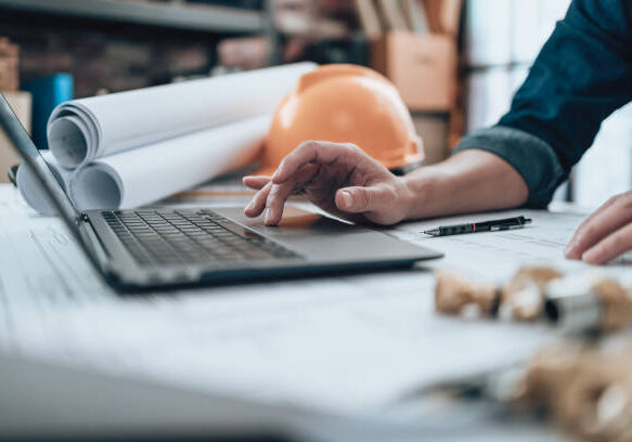 Engineering working with drawings inspection on laptop  in the office and Calculator, triangle ruler, safety glasses, compass, vernier caliper on Blueprint. Engineer, Architect, Industry and factory concept.