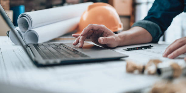 Engineering working with drawings inspection on laptop  in the office and Calculator, triangle ruler, safety glasses, compass, vernier caliper on Blueprint. Engineer, Architect, Industry and factory concept.