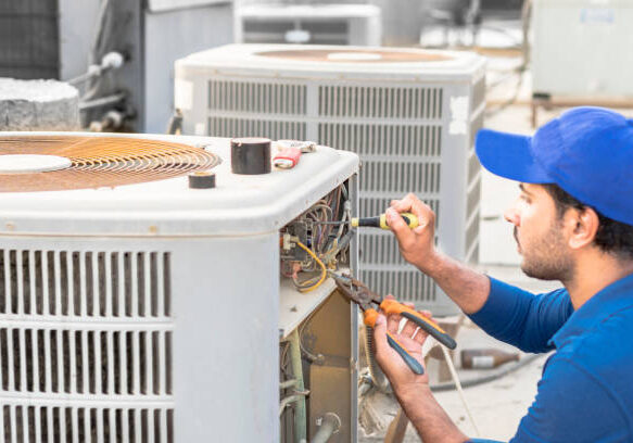 a professional electrician man is fixing the heavy unit of an air conditioner at the roof top of a building and wearing blue uniform and head cap