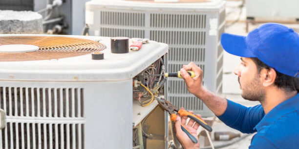 a professional electrician man is fixing the heavy unit of an air conditioner at the roof top of a building and wearing blue uniform and head cap