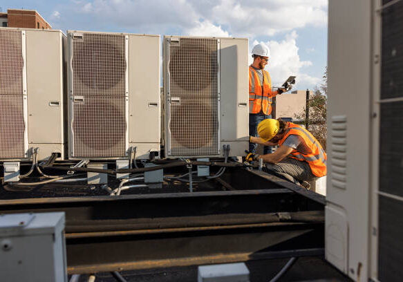 Rooftop air conditioning system inspection. Caucasian white workers check units and log the result with a portable computer.