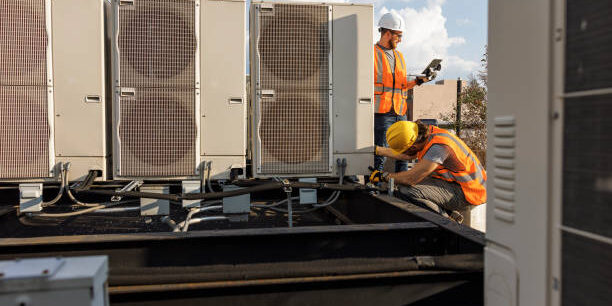 Rooftop air conditioning system inspection. Caucasian white workers check units and log the result with a portable computer.