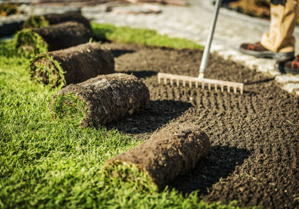 Close Up Of Worker Raking Dirt And Preparing To Install Rolls Of Soil And Turf.