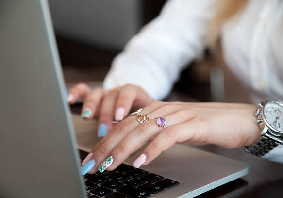 Modern office girl hands on laptop using touch pad and keyboard with rings on fingers and colorful manicure, close up