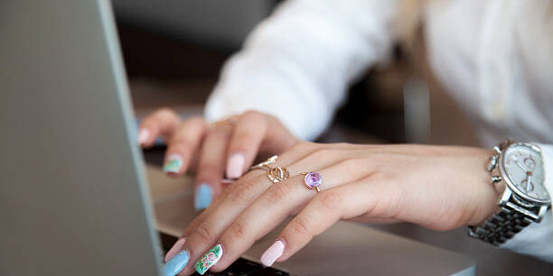 Modern office girl hands on laptop using touch pad and keyboard with rings on fingers and colorful manicure, close up